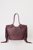 [color: merlot leather] A dark plum leather tote bag with long fringe detailing on the sides and dual top handles, photographed against a clean white studio background.