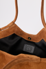 [color: whiskey suede] Close-up of a brown suede shoulder bag with a black interior lining and a visible BTB Los Angeles brand patch.