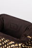 Close-up of the interior of a dark brown clutch or handbag, showing a stitched patch with the embossed letters 'BTB' and a row of gold-tone studs along the edge.
