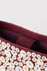 [color:burgundy] Close-up of a burgundy suede or faux-suede bag decorated with large round mother-of-pearl buttons in cream, white, and pale yellow, with a burgundy interior visible.