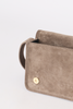 [color:stone suede] A close-up of a taupe-brown suede clutch or wallet-style handbag with a gold-tone snap button and a matching leather loop detail, set against a plain white background.