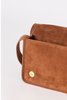 [color:whiskey suede] A close-up of a brown suede clutch or wallet-style bag with a small gold snap button, shown on a plain light background.
