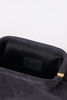 [color: navy suede] Close-up of the interior of a dark gray or black suede clutch bag, showing a black leather patch with the debossed brand name 'BTB' and a gold zipper pull on the right side.
