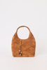 A tan woven suede shoulder bag with a single top handle, gold-tone hardware, and a hanging tassel charm, photographed against a plain light gray background.