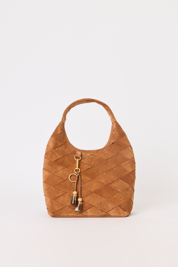 A tan woven suede shoulder bag with a single top handle, gold-tone hardware, and a hanging tassel charm, photographed against a plain light gray background.