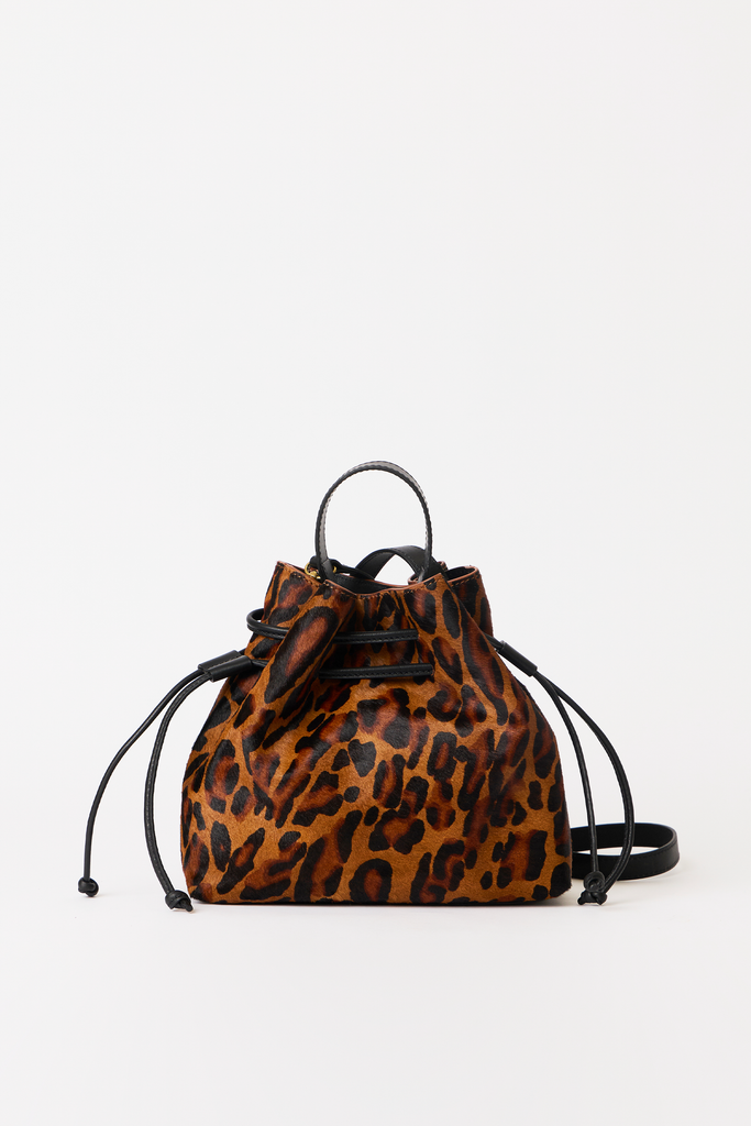 A leopard print mini backpack with black leather straps and a drawstring closure, photographed against a plain white background.