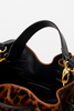 Close-up of a black leather handbag with gold-tone hardware and a leopard-print exterior detail, shown against a light gray background.