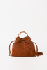 [color: whiskey suede] A brown suede drawstring bucket bag with a braided top handle and a thin shoulder strap, photographed against a plain white background.