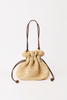 A small woven straw drawstring pouch bag with dark brown leather handles and cords, shown on a clean white background.