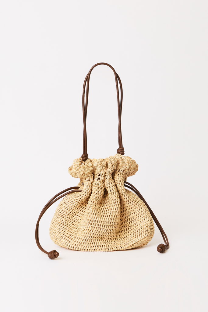 A small woven straw drawstring pouch bag with dark brown leather handles and cords, shown on a clean white background.