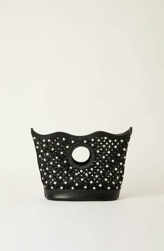 A black leather handbag with a scalloped top edge, a circular cutout handle, and an all-over pattern of white pearl-like studs, photographed against a plain off-white background.
