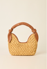 A small woven straw handbag with a tan leather handle and trim, photographed against a plain warm off-white background.