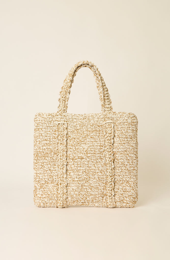 A textured woven tote bag in a natural beige and cream raffia-like material, featuring two top handles and a structured rectangular shape, set against a solid cream background.