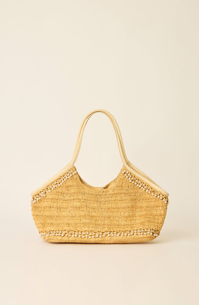 A natural straw woven shoulder bag with light tan leather handles and decorative beaded trim, shown against a solid cream background.