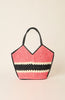 A woven straw tote bag with a pink and black chevron pattern and a horizontal cream stripe, featuring black leather handles, set against a solid light beige background.