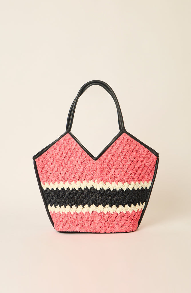 A woven straw tote bag with a pink and black chevron pattern and a horizontal cream stripe, featuring black leather handles, set against a solid light beige background.