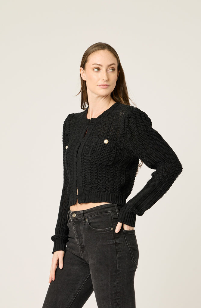 Woman wearing a black knit cardigan with puffed sleeves on a plain background