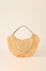 A natural straw crescent-shaped shoulder bag with long fringe detailing and a brown leather handle, set against a solid cream background.