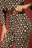 Close-up of a model wearing a matching black and beige floral print two-piece set, featuring a scalloped long-sleeve crop top and high-waisted trousers, set against a solid dark red background.