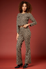 A woman modeling a matching long-sleeve top and wide-leg pants set in a black and beige floral print, styled with a thin brown belt and black pointed-toe heels, against a solid dark red studio backdrop.