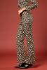 A model is shown from the waist down wearing a black long-sleeve crop top and matching wide-leg pants with a beige floral pattern, paired with black pointed-toe ankle boots, set against a solid dark red studio background.