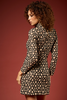 A woman with curly brown hair is shown from the back wearing a long-sleeve mini dress with a beige and black floral pattern, set against a solid dark red studio background.
