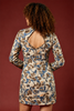 A woman shown from the back wearing a long-sleeve mini dress with a floral pattern in blue, brown, and beige, set against a solid dark red background.