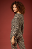 A woman with curly brown hair models a matching two-piece jumpsuit set featuring a black base with a beige floral pattern, posed against a solid dark red studio background.