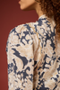 Close-up of a woman wearing a patterned blouse with a navy blue and beige floral design, shown from the side against a solid dark red background.