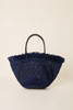 A navy blue woven straw tote bag with a frayed fringe top and a single black handle, photographed against a solid light beige background.